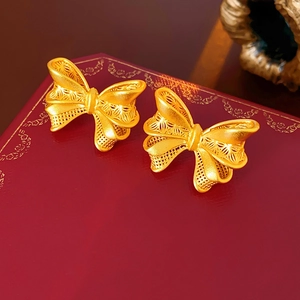 Macro shot of gold-plated hollow bow earrings with detailed filigree on a red leather gift box