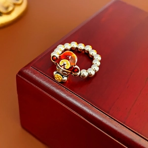 Detail of beaded dragon ring with red enamel zodiac monkey charm on a wooden box