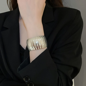 Detailed close-up of a wide silver cuff bracelet with textured vertical stripes on wrist
