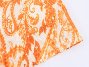 Dettaglio macro del tessuto con stampa paisley arancione e ricami traforati