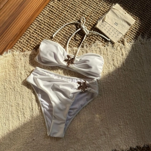 Detailaufnahme des perlweißen Bikinis mit bronzenen Seestern-Metallteilen auf Matte