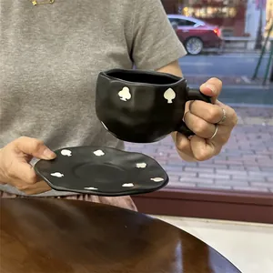 Detail of matte black ceramic cup and saucer set with wavy edges and poker motifs