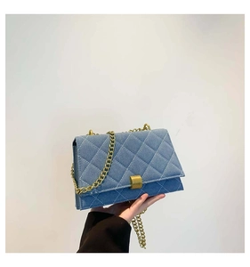 Close-up of blue denim quilted square bag with gold chain strap and lock detail