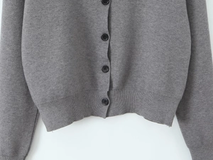 Detail shot of grey knitted cardigan showing black buttons and ribbed hem texture