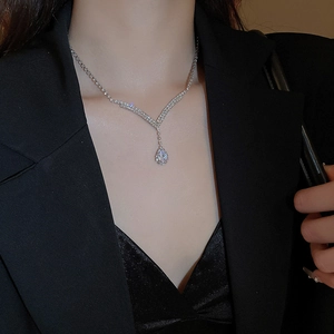 Detail of silver V-shaped necklace with a teardrop crystal on a model in a black suit