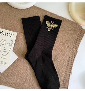 Detailed view of black knit mid-calf socks with intricate bee embroidery and wings
