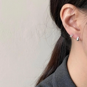Detail of silver drop and textured bar stud earrings worn on a model's ear
