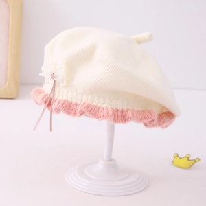 Detail of baby girl knitted beret featuring pink ruffled edges and a white lace bow