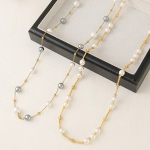 Close-up of a long gold chain necklace with white and grey pearls on a jewelry box
