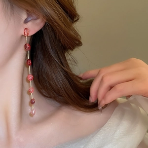Detailed view of long strawberry crystal tassel earrings with red gradient beads on a model