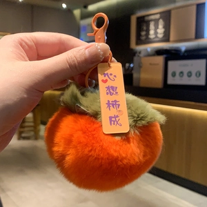 Close-up of a plush orange persimmon keychain with a green leaf and heart-warming tag