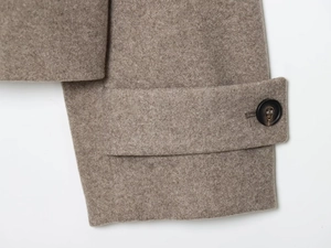 Détail du poignet d'un manteau en laine avec patte décorative et bouton rond texturé