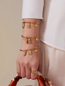 Close-up of golden ocean-themed bangles with shell charms and a sparkling stone ring