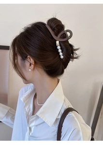 Détail de pince à cheveux marron foncé avec perles et étiquette dorée sur cheveux