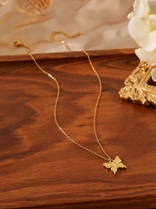 Detail shot of a golden butterfly pendant necklace resting on a premium wooden tray