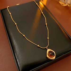 Macro shot of irregular golden teardrop pendant with brown tiger eye stone on snake chain