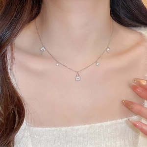 Close-up of silver necklace set with lock, key, and pearl pendants on a female model