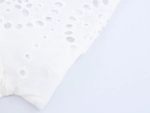 Detailed close-up of white cotton fabric featuring intricate floral eyelet embroidery patterns