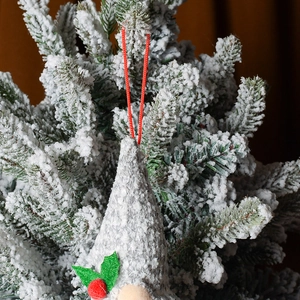 Nahaufnahme eines grauen Strick-Weihnachtswichtels an einem verschneiten Tannenzweig