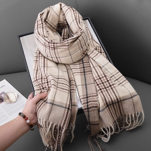 Cozy beige plaid scarf with fringe tassels draped over a sofa with stylish lifestyle props