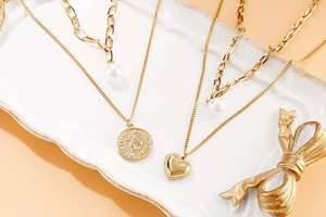 Détail d'un collier doré multicouche avec perle baroque, cœur et pendentif pièce