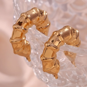Macro detail of gold-plated bamboo texture hoop earrings on a decorative glass bowl