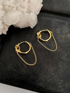 Detailed view of gold knot chain earrings on dark stone background with crystal