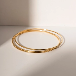 Minimalist gold titanium steel thin bangles stacked on white surface in natural light