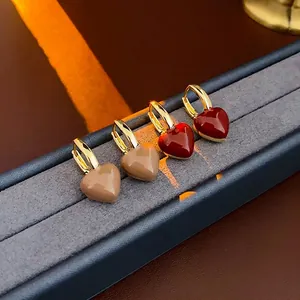 Elegant gold plated heart drop earrings in deep red and khaki on a velvet jewelry display
