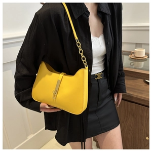Detail of yellow leather shoulder bag with gold metal clasp and chain strap on model