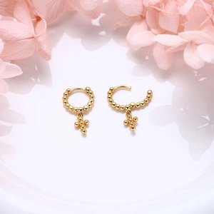 Close-up of gold beaded hoop earrings with cross pendants on a floral background