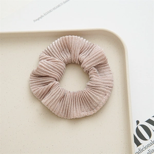 Detail showing champagne pleated fabric scrunchie with glossy texture on beige tray