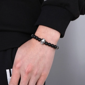 Detail view of natural stone beaded bracelet with a silver skull charm on male wrist