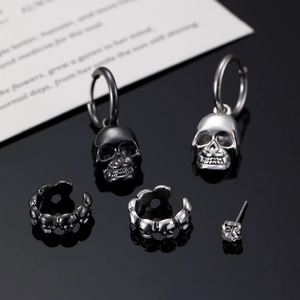 Gothic skull earring set with black and silver cuffs and studs on reflective surface