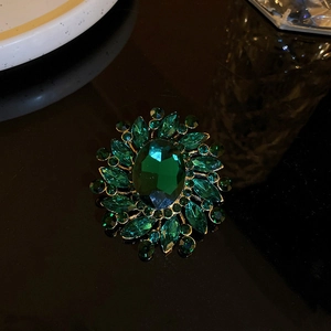 Close-up of emerald green oval crystal flower brooch with gold alloy base and green rhinestones