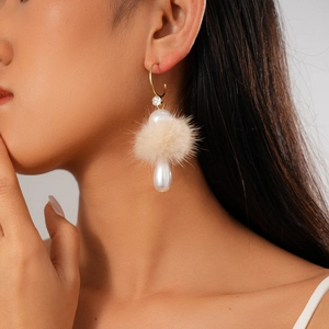 Close-up of elegant C-shaped gold earrings with beige fur pompom and white pearl charm
