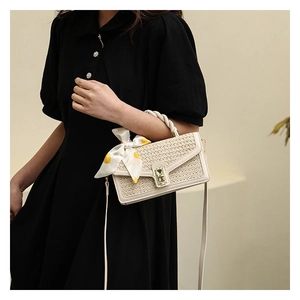 Detail of cream woven handbag with yellow silk scarf bow and gold clasp on black dress