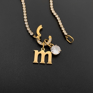 Close-up of gold titanium steel necklace with sparkling rhinestone and letter m charm