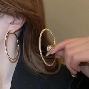 Close-up of luxury gold hoop earrings with sparkling rhinestones worn by a model