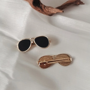 Detail view of two gold-framed sunglasses hair clips on white silk background