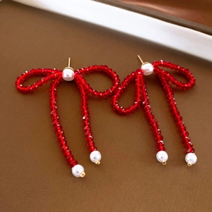 Close-up of red beaded bow earrings with white pearls on a textured background