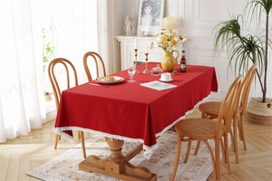 Detail of red cotton tablecloth with white lace edges on a wooden dining table