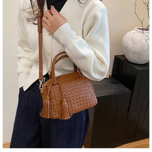 Detail of woven brown handbag with leather tassels shown in a minimalist interior setting