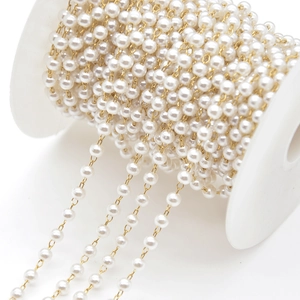 Macro shot of white imitation pearl chain with gold metal links on a spool for DIY jewelry