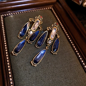Vintage gold teardrop earrings with blue and clear crystals on green fabric
