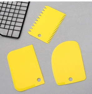 Three yellow plastic dough scrapers with straight, serrated, and rounded edges for baking