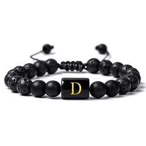 Gros plan des perles de lave volcanique et du charme lettre D dorée sur le bracelet
