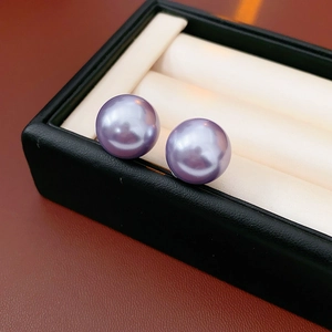 Detailed close-up of large round purple pearl earrings in a premium jewelry box