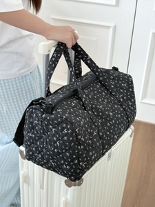 Borsa da viaggio trapuntata a fiori posizionata sulla maniglia di una valigia