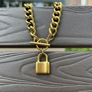 Detail of gold Cuban chain necklace with industrial T-bar clasp and smooth padlock pendant